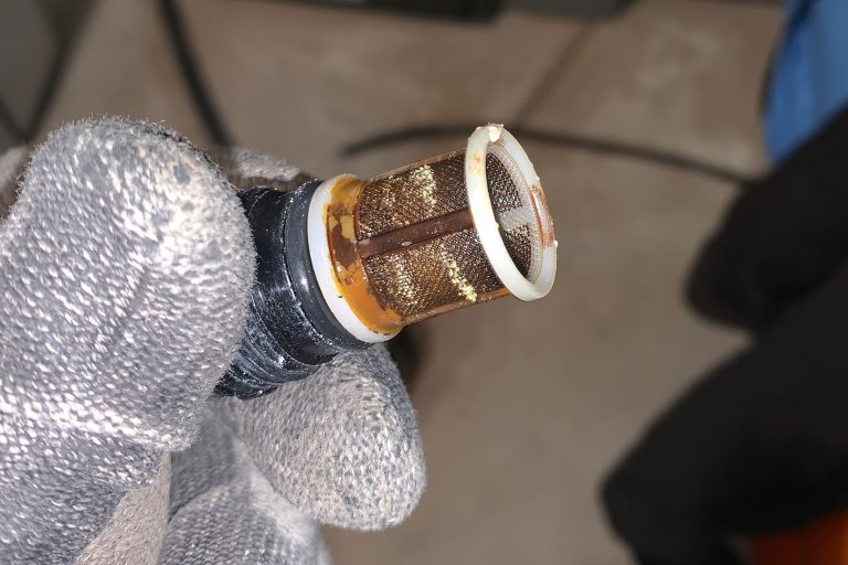 Close-up of a clogged water heater filter screen showing mineral buildup and sediment accumulation from hard water