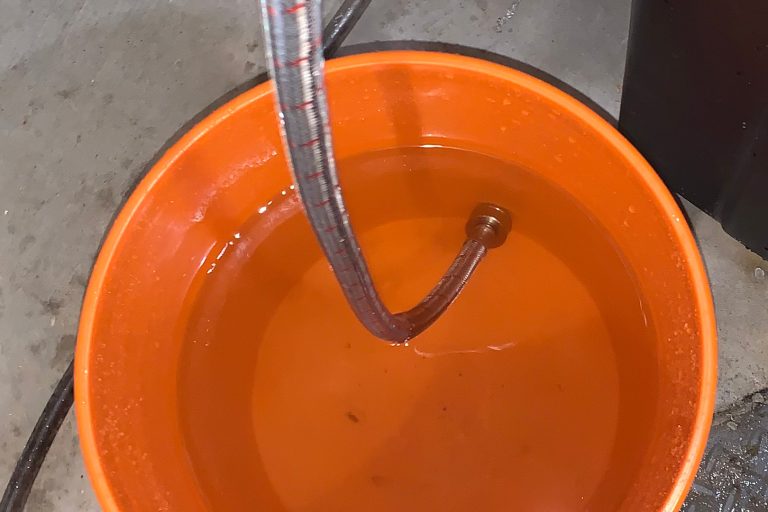 Clean orange bucket with clear water and maintenance hose after completing a tankless water heater flush